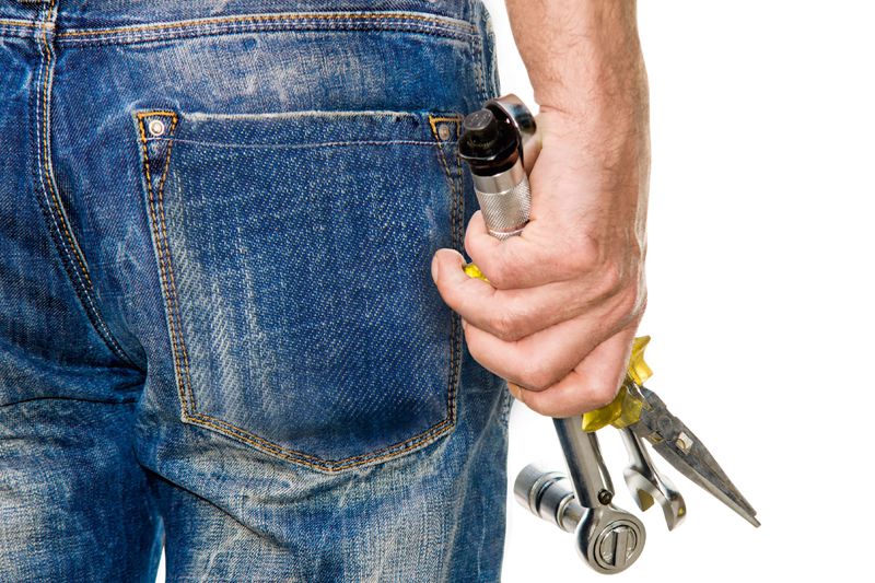 Nahaufnahme einer Person in Jeans, die verschiedene Werkzeuge wie Zange und Schraubenschlüssel in der Hand hält.